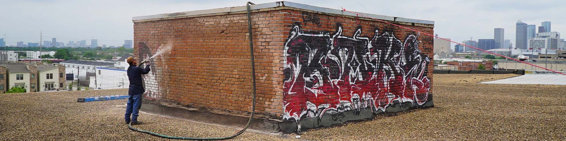 A man is standing in front of a brick wall with graffiti on it.